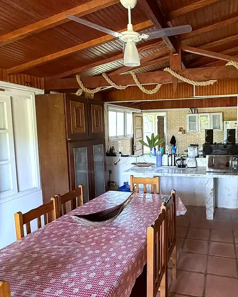 Mesa de jantar com cadeiras de madeira, ventilador de teto e a cozinha ao fundo