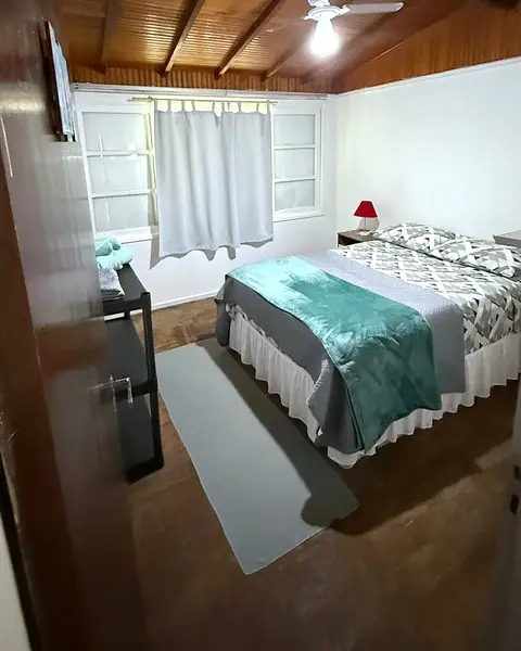 Quarto com cama de casal arrumada e janela com cortina